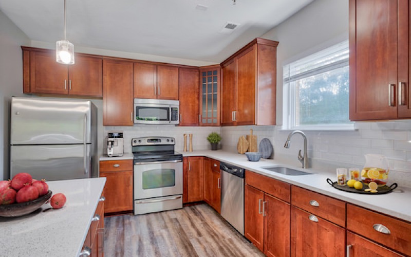 Newly renovated kitchen with white quartz counter tops, brown cabinets, large window and backsplash 